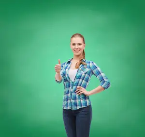 A smiling woman wearing a plaid shirt and jeans gives a thumbs up in front of a green chalkboard background.
