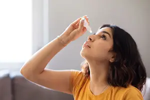 A woman using eye drops in a room