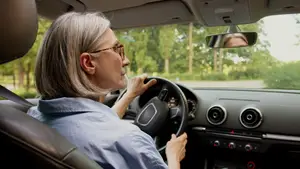 An older woman with glasses driving a car in the daytime