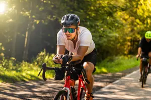 Two men riding bicycles on a dirt path surrounded by trees