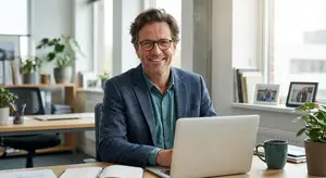 Man wearing glasses and a suit jacket working on a laptop in an office.