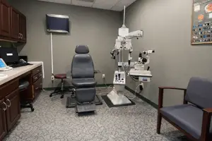 A room with a medical examination chair, an ophthalmoscope, and a computer monitor, all set up for eye examinations