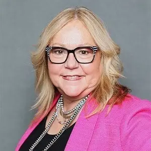 Portrait of a woman with blonde hair, wearing glasses, a pink blazer, and a necklace