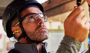 A man in a helmet, glasses, and ear protection is holding a tool in his hand.
