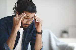 Man sitting on a couch with his hands on his forehead, looking down.