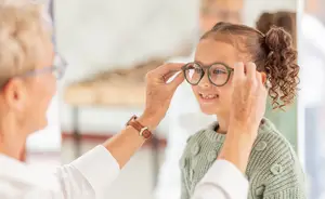 A woman is adjusting a child's glasses in a medical office