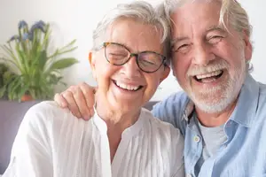 A senior couple smiling together with a potted plant behind them