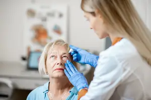 An elderly woman receiving eye drops from a medical professional in a clinic setting