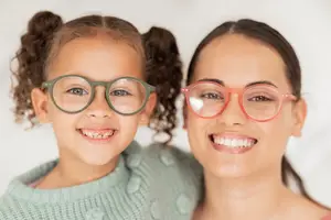 A girl and a woman are smiling and posing for a photo while wearing glasses.