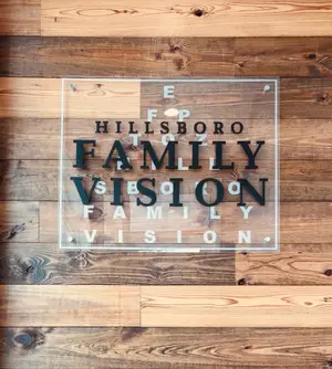 Wooden sign with black text on a wooden background reads 'Hillsboro Family Vision'.