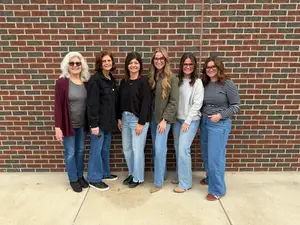 Six women pose for a photo in front of a brick wall