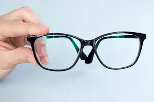 A person holding a pair of glasses with a black frame and green temple tips