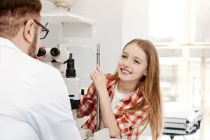 An eye doctor examining a young girl's eyes with an ophthalmoscope.
