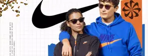 A man and a woman wearing sunglasses and hoodies are standing close to each other and smiling. They are probably promoting a product. The man is wearing a blue hoodie with the Nike logo on it, while the woman is wearing a black hoodie. Behind them is a white background with the Nike logo and some golden confetti. There is a blue and orange design on the right side, and the background is white with a grid-like pattern.