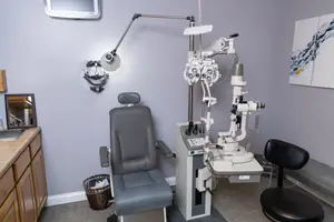 A medical room has a chair, a desk, and an eye examination machine with a lamp.
