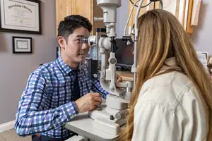 An optometrist adjusts the settings on an ophthalmoscope while examining a patient's eye