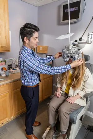 An optometrist is adjusting the phoropter for a patient in an examination room.