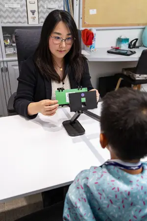 A woman in a classroom is showing a device to a young boy