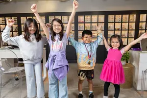 Four young children with glasses pose for a photo in a room with shelves of eyeglasses in the background