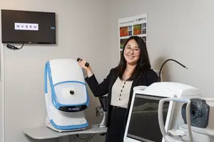 A woman is standing next to a machine that is probably an eye scanning machine.