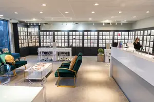 Interior view of a modern optometrist's office with a woman standing at the front desk and various furniture and decor.