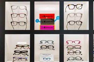 A display of various eyeglasses from La.Eyeworks, arranged in multiple glass cases with a black frame and white background, showcasing different styles and colors.