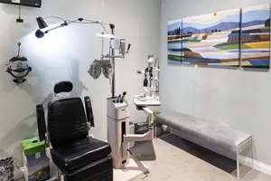An empty optometrist's office with an examination chair, examination light, and a bench