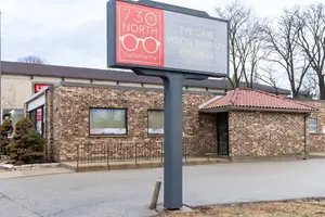 730 North Optometry sign in front of a brick building with a metal fence and trees in the background