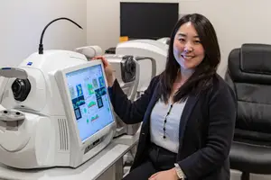 Woman sitting in front of a monitor with an eye scanner and smiling at the camera