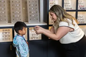 A woman is showing a child a pair of glasses in a store