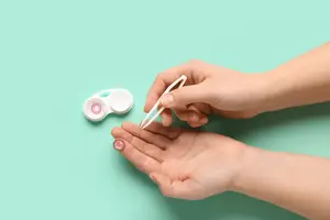 An adult woman is using a pair of tweezers to handle a contact lens.