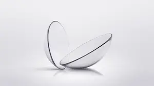 A transparent glass contact lens with a blue border rests on a white background, showcasing its clear and smooth surface.