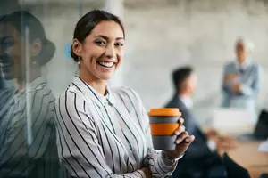 A smiling woman in a striped shirt holding a coffee cup in an office setting