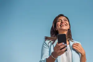 A smiling woman holding a cell phone and looking up