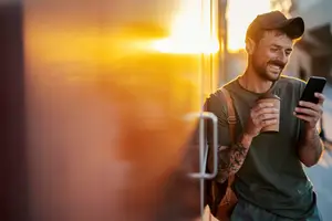 A man standing on the side of the road is holding a cup of coffee and looking at his phone