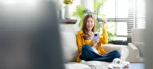 A woman sitting on a couch holding a phone and smiling