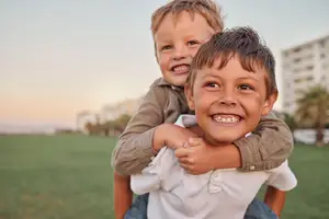 Two boys are smiling and posing for a photo on a grassy field with buildings in the background