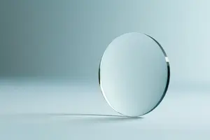 A shiny round glass lens with a silver border is placed on a white surface