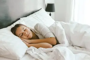 A young woman is sleeping in bed under a white blanket