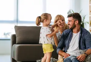 A family is sitting on the couch in the living room, and a girl is standing near them, smiling.