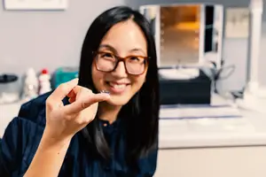 Asian woman in glasses shows a fingernail clipper to the camera while smiling
