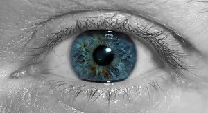 Close-up view of a human eye with blue iris and brown spots.