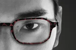 A close-up of a person's eye wearing glasses with a red and black patterned frame.