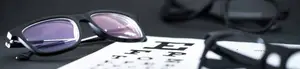 A pair of black sunglasses with purple lenses and a blurry eye chart in the background