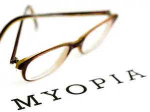 Pair of eyeglasses with a blurry image of the word myopia on a white background