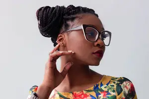 A woman with braided hair is posing for a photo while wearing glasses and a floral dress.