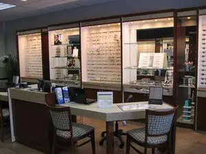 An optometrist office with a desk, chairs, and a shelf with eyeglasses on display.