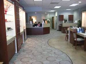 An image of an empty office waiting room with a curved carpet, wooden furniture, and a receptionist desk in the distance