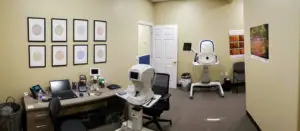 A medical office room with several pieces of equipment on the desk and framed pictures on the wall