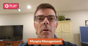 The man is speaking about myopia management while standing in a room with a TV and cabinet.